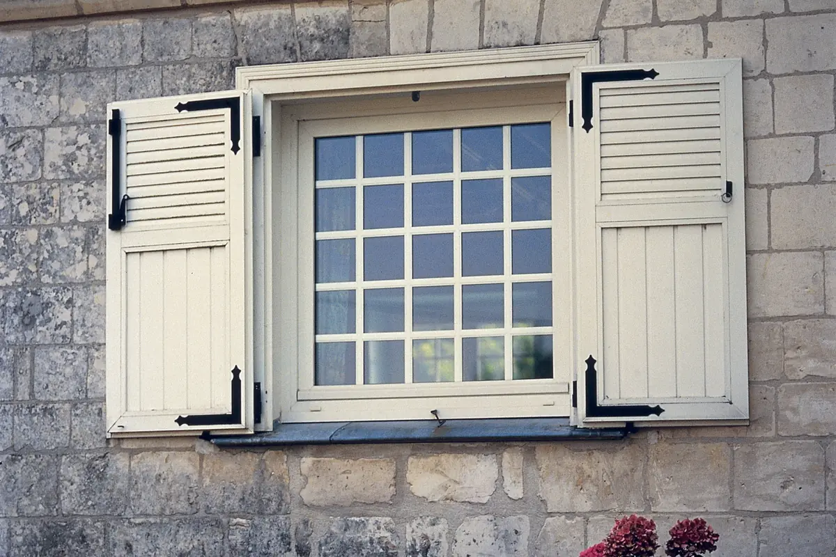 Cream casement window with shutters in a stone wall