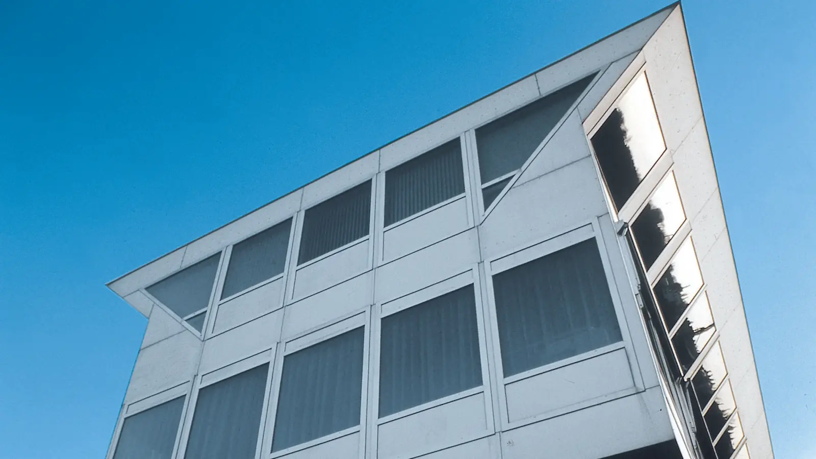Glazed facade with angled windows against a blue sky